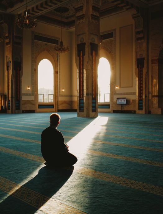A person in prayer inside Sendayan mosque, illuminated by soft sunlight highlighting the serene architecture.